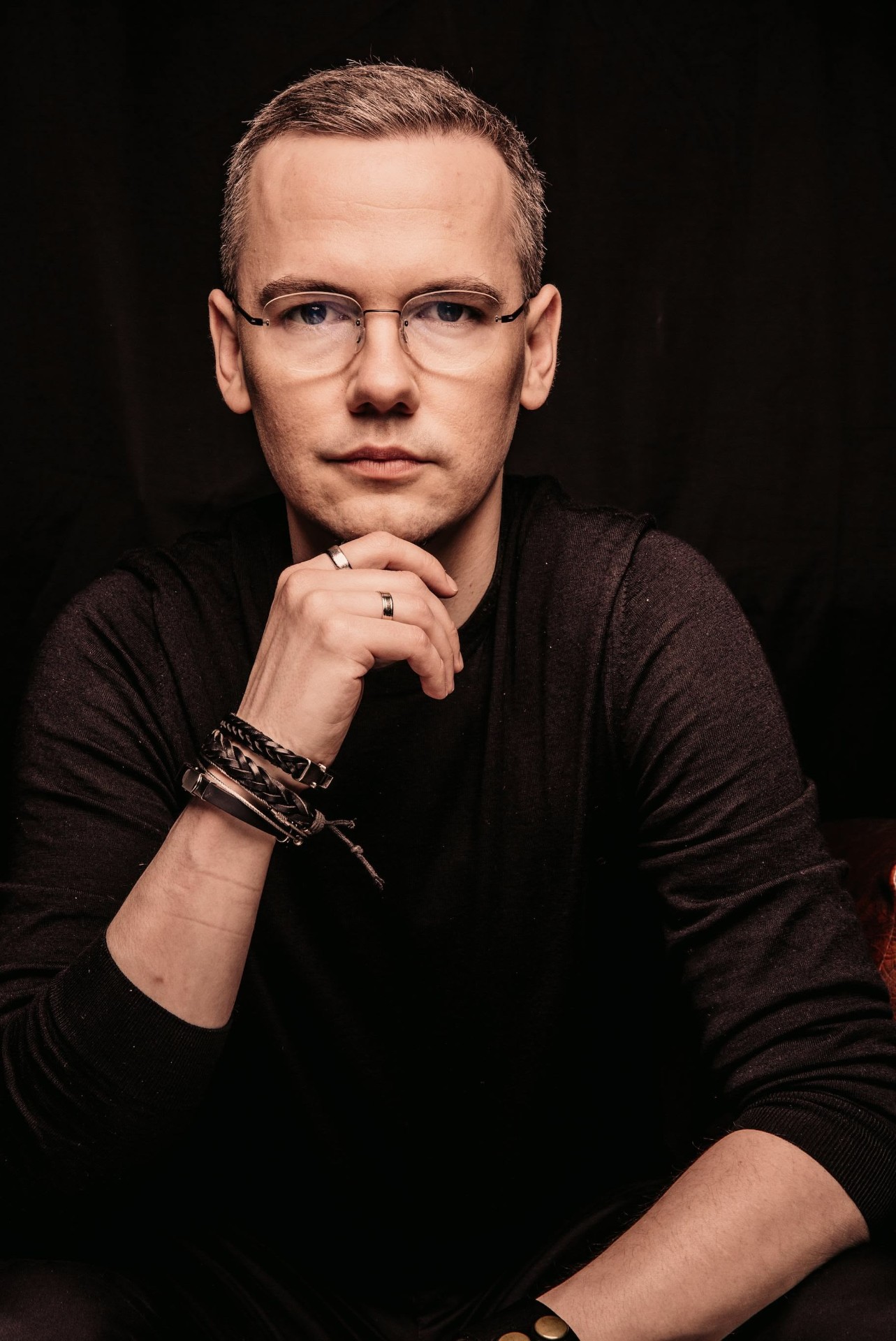 Ludwik C. Siadlak w czarnej bluzie i okularach, z ręką pod brodą, patrzy prosto w obiektyw